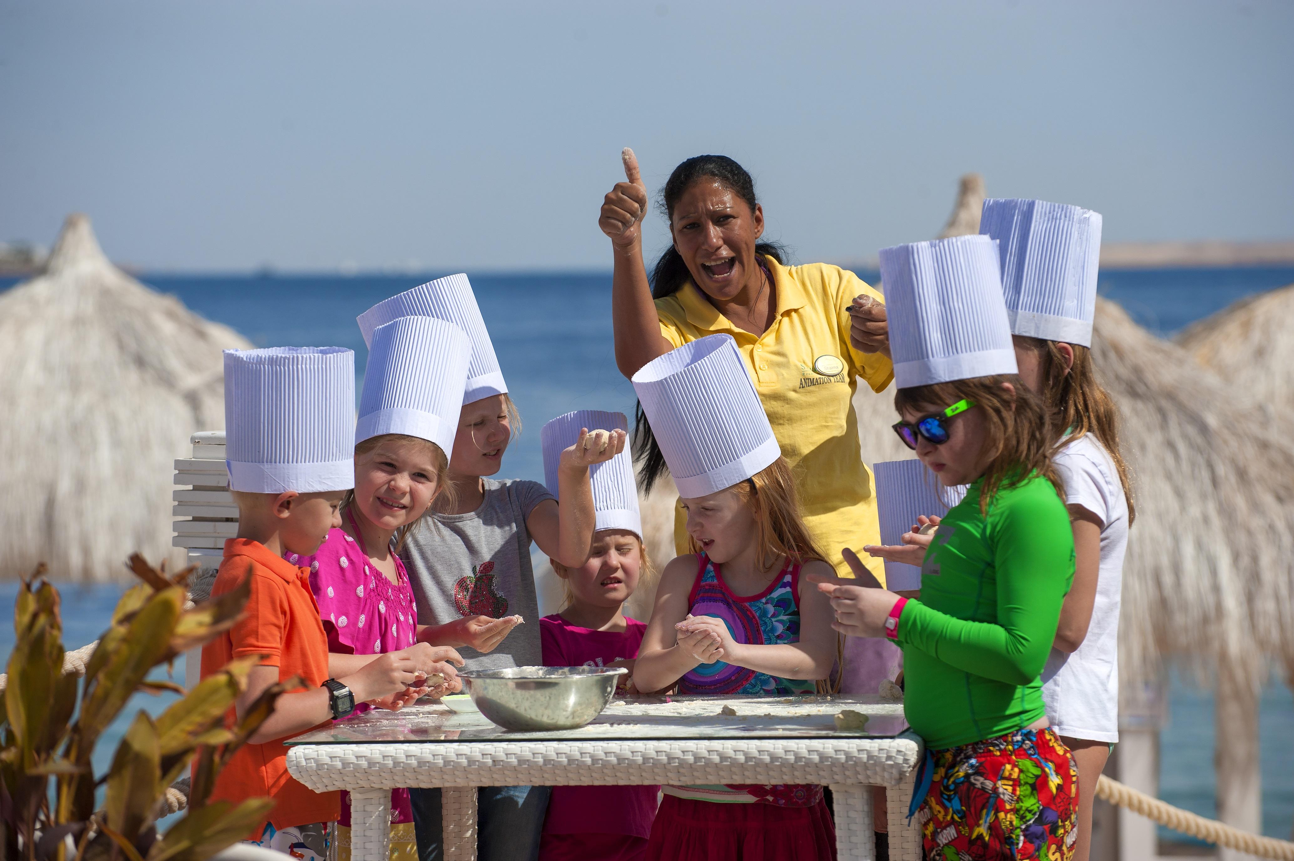 Sunrise Arabian Beach Resort Sharm el Sheikh Esterno foto The photo shows a group of children, all wearing white chef hats, gathered around a table. They appear to be engaged in a cooking activity, possibly making something together. A woman, likely a instructor or leader, is standing among them, giving a t