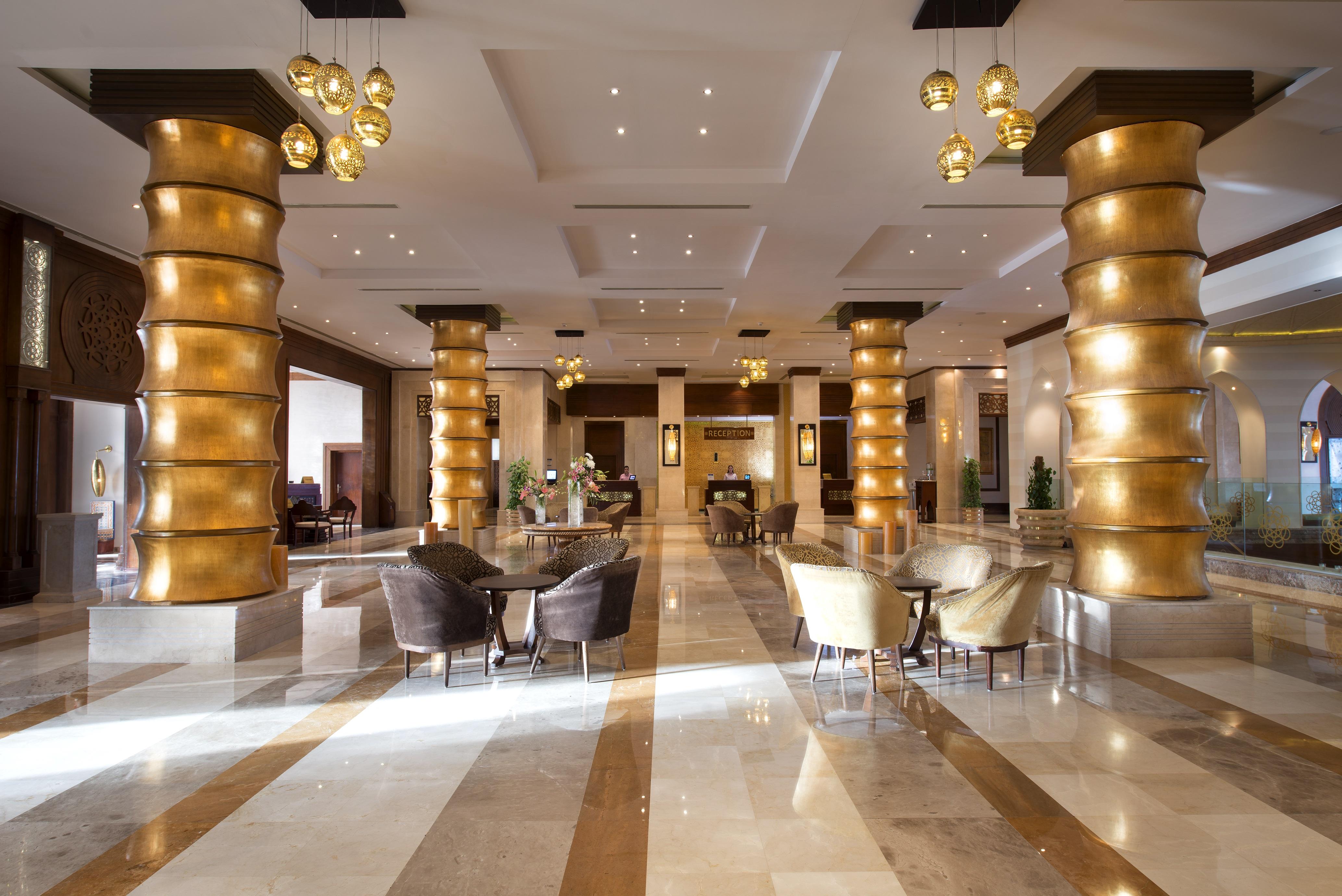 Sunrise Arabian Beach Resort Sharm el Sheikh Esterno foto The photo shows a spacious hotel lobby with elegant decor. There are tall, golden columns that create a striking visual effect. The floor features a mix of light and dark marble tiles, adding to the luxurious ambiance. A variety of seating is arrange