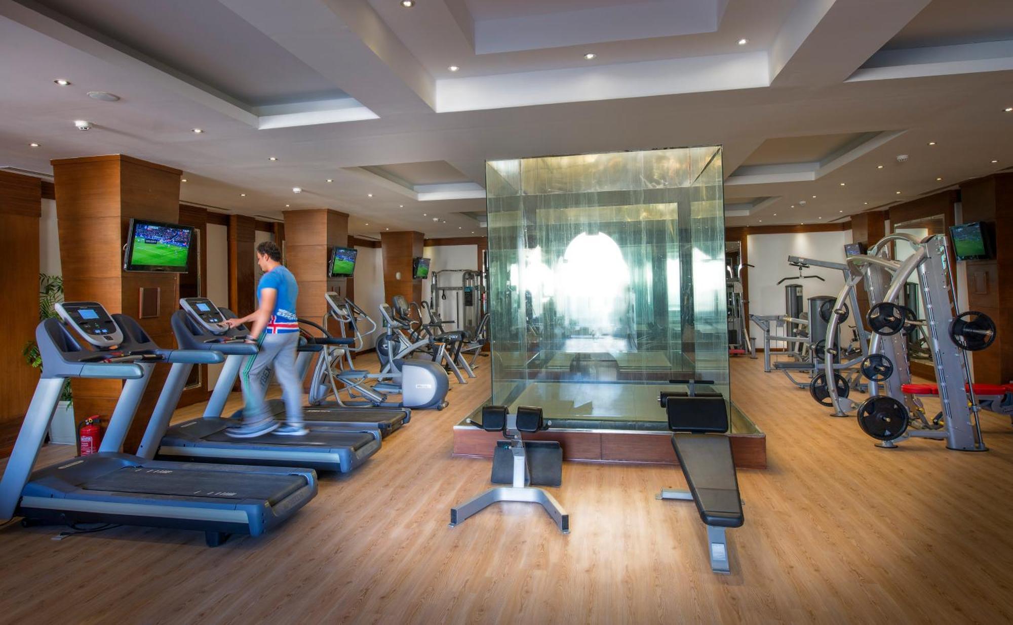 Sunrise Arabian Beach Resort Sharm el Sheikh Esterno foto The photo shows a modern gym with various exercise equipment. On the left side, there are treadmills, with a person walking on one of them. In the center, there's a glass-walled space, which likely serves as a private area for workouts or classes. Th